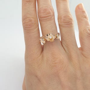 May include: A rose gold ring with three delicate flower designs, each with a small diamond in the center.