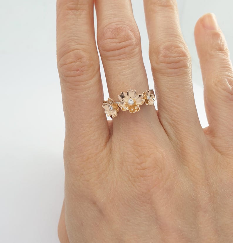 May include: A rose gold ring with three delicate flower designs, each with a small diamond in the center.