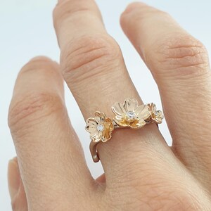 May include: A gold ring with three delicate flower designs, each with a small diamond in the center.