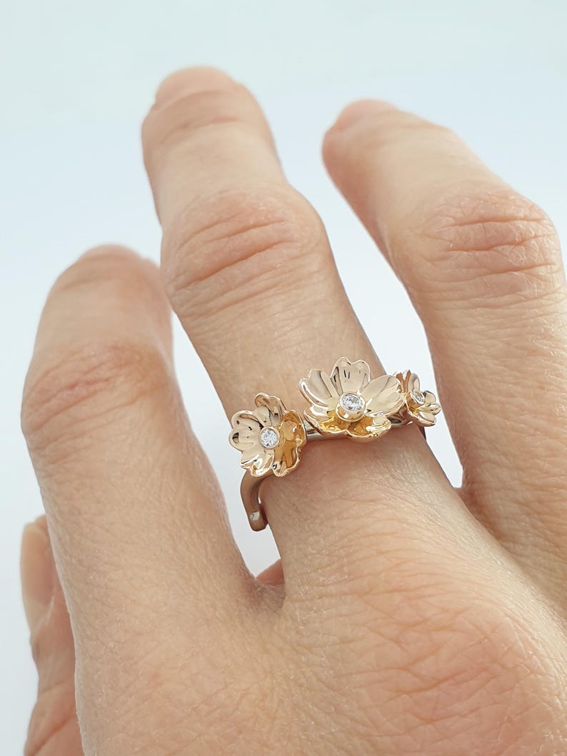 May include: A gold ring with three delicate flower designs, each with a small diamond in the center.