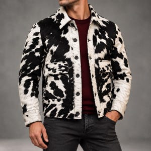 May include: A long-sleeve jacket featuring a black and white cow print pattern, a pointed collar, and a front button closure. The jacket includes two chest pockets with buttoned flaps and long sleeves with buttoned cuffs, worn over a dark red shirt.