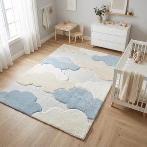 May include: A rectangular area rug featuring a repeating pattern of soft, tufted clouds in shades of light blue, cream, and off-white. The rug has a textured, plush pile surface and is positioned on a light-toned wooden floor in a room.