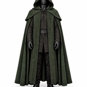 Può includere: Un mantello con cappuccio verde oliva scuro indossato sopra una tunica nera a maniche lunghe con allacciatura frontale, una cintura nera con fibbia rettangolare, pantaloni neri e stivali neri. Il mantello presenta un ampio colletto e arriva fino a terra.