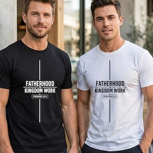 Puede incluir: Una camiseta negra de manga corta y una camiseta blanca de manga corta, cada una con un gráfico de línea vertical y el texto FATHERHOOD IS KINGDOM WORK y PROVERBS 22:6 impreso en una fuente negrita sin remates en el área del pecho.