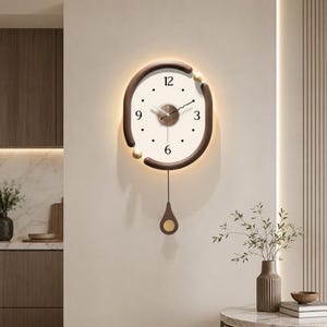 May include: A wall clock with a circular white face, black numerals at 3, 6, 9, and 12, and thin black hands. The clock is framed by a dark brown curved border with gold accents and features a matching dark brown pendulum with a gold circular weight.