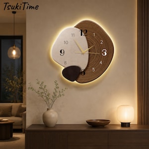 Könnte beinhalten: Eine Wanduhr mit asymmetrischem Design, bestehend aus einem hellbeigen, strukturierten Teil, einem dunkelbraunen Holzmaserungsteil und einem kleinen dunkelbraunen Akzentstück. Das Zifferblatt zeigt schwarze Ziffern und goldene Zeiger.