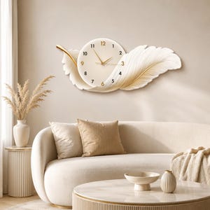 May include: A wall clock featuring a circular cream-colored face with black numerals and gold hands, integrated into a sculptural white feather design with gold accents. The clock face displays the numbers 1 through 12 in a simple sans-serif font.