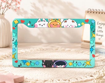 May include: A rectangular teal license plate frame featuring a colorful graphic print of various cartoon characters, red hearts, yellow starbursts, blue musical notes, and light blue cloud shapes distributed across the entire border surface.