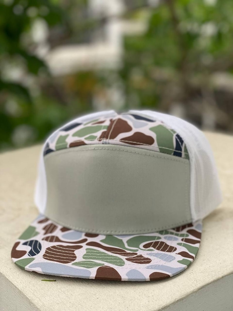 May include: A trucker hat with a camouflage pattern on the bill and top, featuring shades of brown, green, and blue. The front panel is a solid light green, and the back is white mesh. A stylish accessory for outdoor activities.