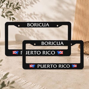 May include: Two black license plate frames with white text that reads "BORICUA" and "PUERTO RICO". The frames have the Puerto Rican flag on them. One frame is larger than the other.