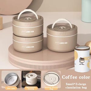May include: Two round, coffee-colored lunch boxes with white handles and lids, featuring the text LUNCH BOX. Includes a smaller white container with the text EAT WELL and a cartoon icon. Features include a 304 liner, microwave heating, and a sealing silicone ring.