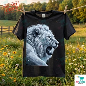 May include: Black t-shirt featuring a detailed illustration of a roaring white lion. The lion's mane and face are intricately designed, with a focus on the open mouth and sharp teeth. The shirt is hanging on a clothesline outdoors.