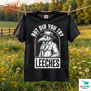 Puede incluir: Camiseta negra con un gráfico de un médico de la peste con sombrero y abrigo, con el texto blanco "BUT DID YOU TRY LEECHES". La camiseta está colgada en un tendedero al aire libre.