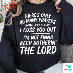 Puede incluir: Sudadera negra con texto blanco: "THERE'S ONLY SO MANY PRAYERS IMMA PRAY BEFORE I CUSS YOU OUT I'M NOT FINNA KEEP BOTHERIN' THE LORD." La sudadera tiene cuello redondo.