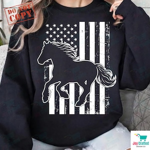 Könnte beinhalten: Ein schwarzes Langarm-Sweatshirt mit einem großen weißen Grafikdruck auf der Vorderseite. Das Design zeigt die Silhouette eines Pferdes in Bewegung, überlagert von einem abgenutzten, verwitterten amerikanischen Flaggendesign mit Sternen und Streifen.