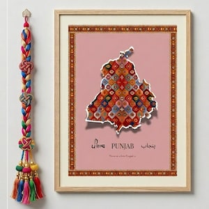 May include: A framed print featuring a map of Punjab with a colorful geometric pattern. The print is set against a pink background and includes text in multiple languages. A decorative tassel hangs on the left.