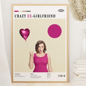 Könnte beinhalten: Gerahmtes Poster für die Fernsehserie "Crazy Ex-Girlfriend" mit einer Frau in einem rosa Kleid, die einen herzförmigen Ballon hält. Das Poster hat einen beigefarbenen Hintergrund mit einem rosa Kreis und dem Titel der Show. Das Jahr 12015 ist sichtbar.