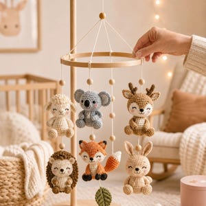 May include: A wooden baby mobile featuring six crocheted animal figures: a cream sheep, a grey koala, a brown deer, a brown hedgehog, an orange and white fox, and a tan rabbit, all suspended from a circular wooden frame with small wooden beads.