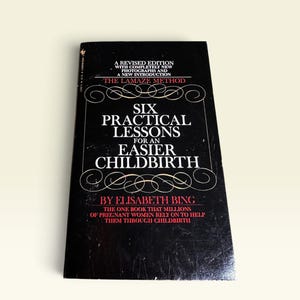 May include: A black paperback book titled Six Practical Lessons for an Easier Childbirth by Elisabeth Bing. The cover features white and red text, decorative white line flourishes, and the subtitle The Lamaze Method in red lettering.