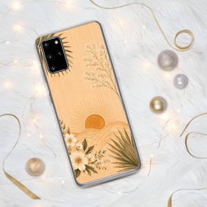 Peut inclure: Une coque de téléphone rectangulaire avec un fond en grain de bois clair présentant un motif imprimé de soleil se levant sur des collines, entouré d'illustrations botaniques de fleurs, de feuilles de palmier et de brindilles dans des tons orange, marron et crème.