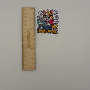 May include: A die-cut sticker featuring a cartoon corgi wearing glasses and a red hoodie, typing on a laptop with papers flying around. The text reads AI DID MY HOMEWORK. A wooden ruler is placed next to the sticker, showing it is about 7.5 cm tall.