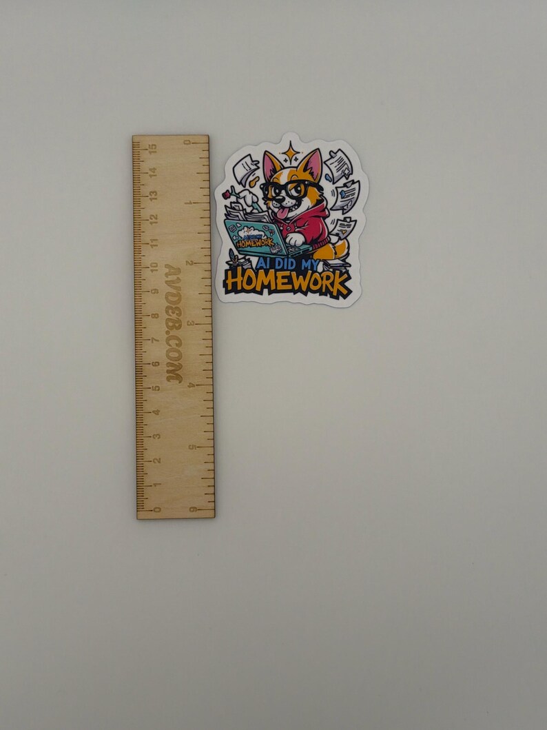 May include: A die-cut sticker featuring a cartoon corgi wearing glasses and a red hoodie, typing on a laptop with papers flying around. The text reads AI DID MY HOMEWORK. A wooden ruler is placed next to the sticker, showing it is about 7.5 cm tall.