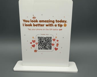May include: A white rectangular acrylic sign with a base, featuring the brown text "You look amazing today. I look better with a tip" and "Tap your phone on the QR below". The design includes red hearts, coffee cup icons, and a central QR code.