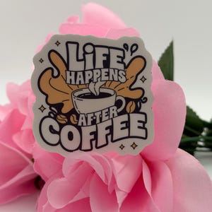 May include: A white die-cut sticker featuring a black and tan graphic of a coffee cup with steam rising. The text reads "LIFE HAPPENS AFTER COFFEE" in bold, stylised black lettering. The design includes small star accents and a coffee bean icon.
