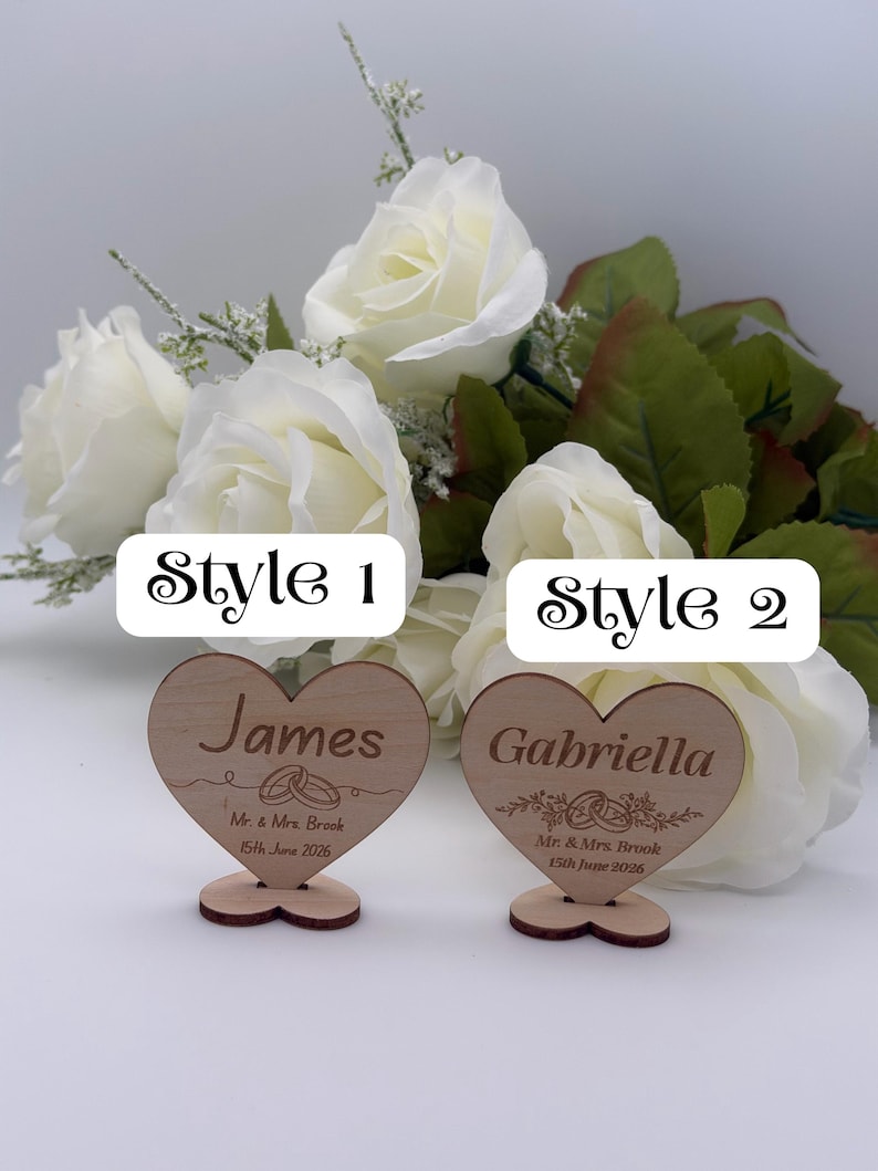 May include: Two heart-shaped wooden place cards with stands. The left card features the name James, the text Mr. & Mrs. Brook, and the date 15th June 2026. The right card features the name Gabriella, the same text, and the date 15th June 2026.