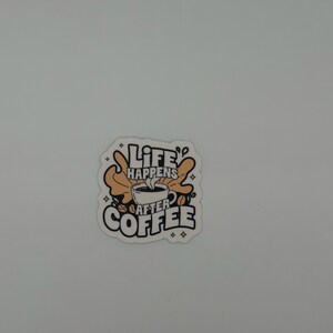 May include: A die-cut sticker featuring a central illustration of a steaming coffee cup surrounded by tan abstract shapes and coffee beans. The text reads Life Happens After Coffee in bold black lettering with small star accents on a white background.