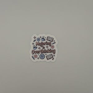 May include: A die-cut sticker featuring the text Majoring in Overthinking in a pink and brown font. The design includes blue coffee mugs, open books, pencils, four-pointed stars, and blue and pink sad face emojis scattered around the lettering.