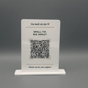 May include: A white rectangular acrylic sign with a stand featuring the text You made my day with a heart icon, the words SMALL TIP, BIG IMPACT, a central QR code, and the text Thank you for your support printed in black and gold ink.