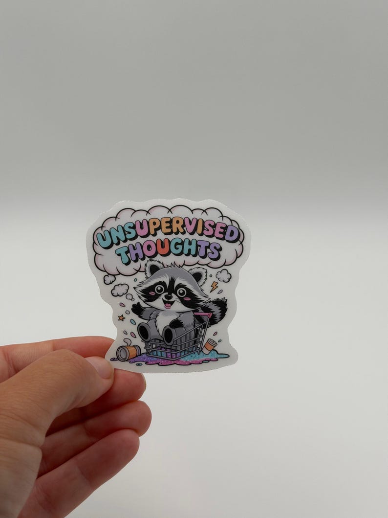 May include: A die-cut sticker featuring a cartoon raccoon sitting in a shopping cart with a pink, blue, and yellow thought bubble above its head containing the text UNSUPERVISED THOUGHTS in colorful letters, surrounded by scattered trash items.