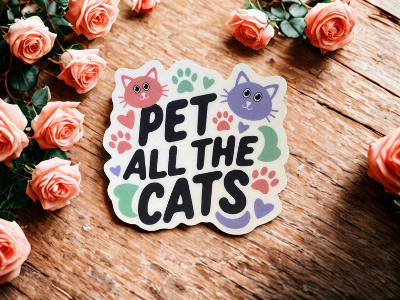 May include: A sticker with the text "PET ALL THE CATS" in black, with cat faces, paw prints, and hearts. The sticker is surrounded by peach-colored roses on a wooden surface.