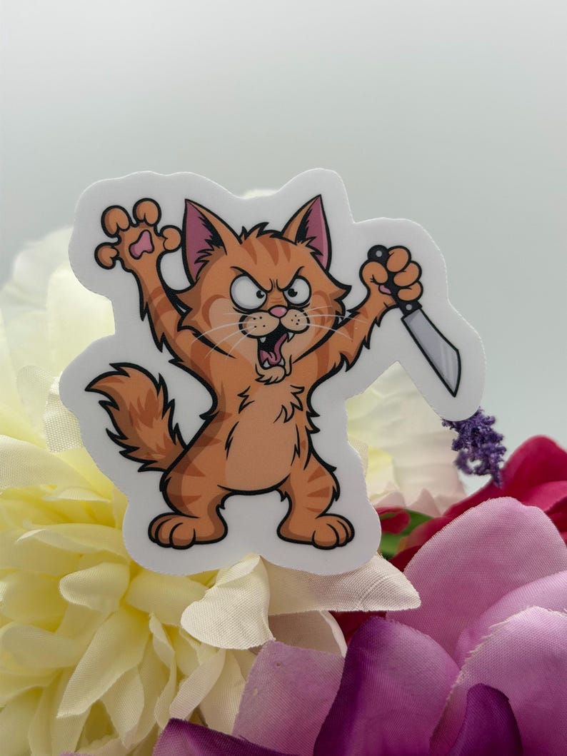 May include: A die-cut vinyl sticker featuring a cartoon orange tabby cat with a fierce expression, baring its teeth and claws. The cat is standing on its hind legs, holding a small silver kitchen knife in one paw and raising the other paw.