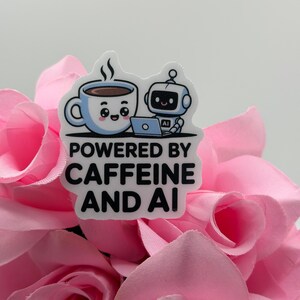 May include: A die-cut sticker featuring a cartoon light blue coffee mug with a smiling face and a small white robot using a laptop. The text reads POWERED BY CAFFEINE AND AI in bold black letters. The design is set against a background of pink roses.
