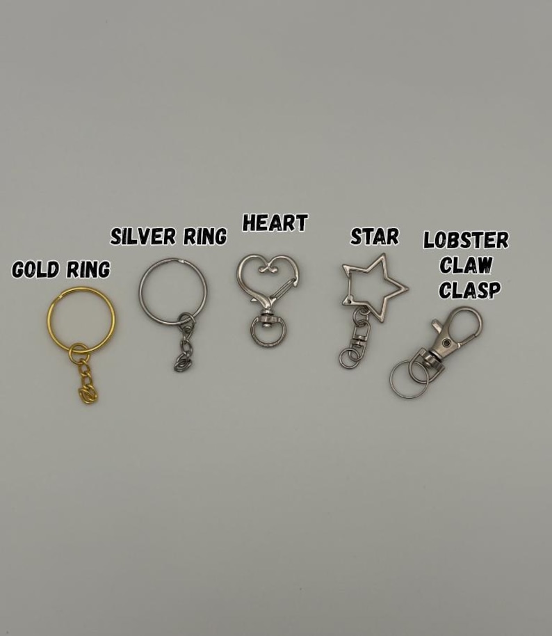 May include: A collection of metal keychain hardware including a gold ring, a silver ring, a heart-shaped clasp, a star-shaped clasp, and a lobster claw clasp. Each item is labeled with its corresponding name in black text above the hardware.