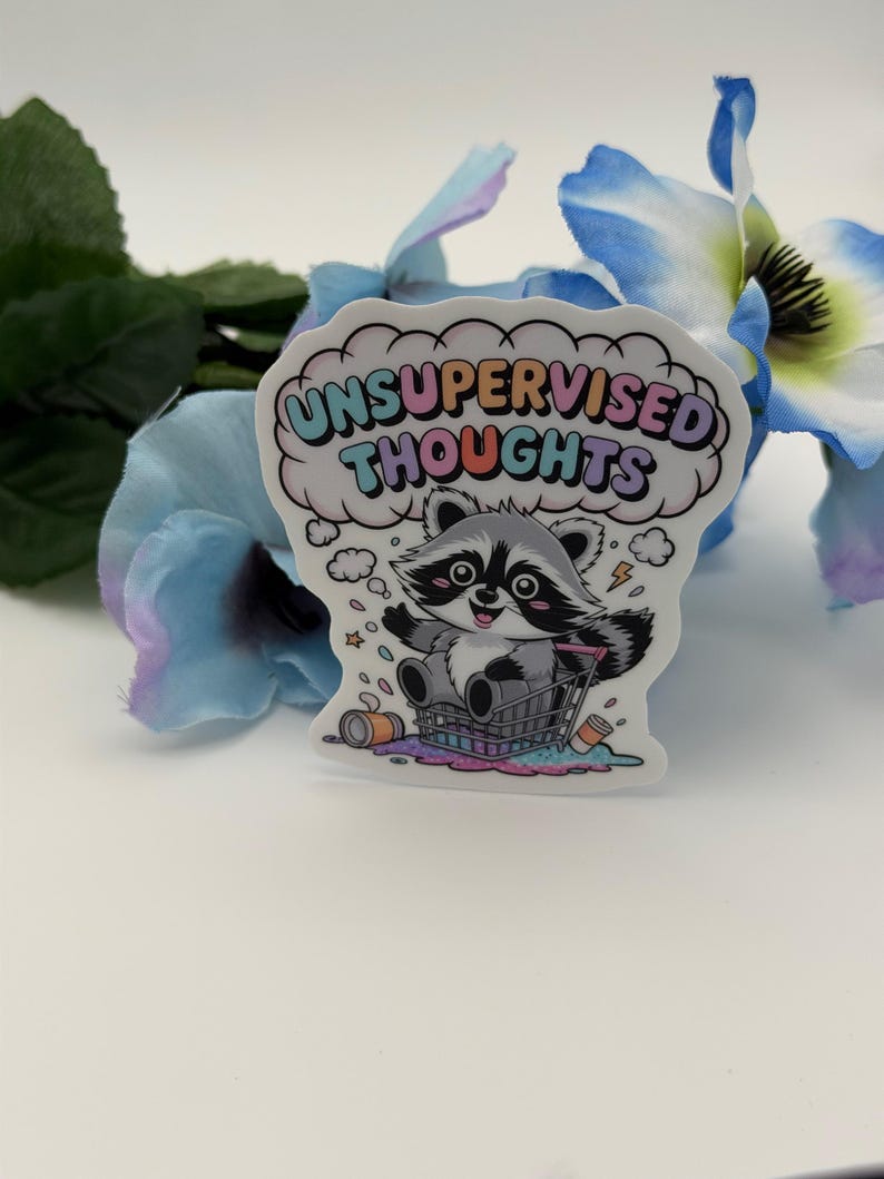 May include: A die-cut sticker featuring a cartoon raccoon sitting in a shopping cart with the text UNSUPERVISED THOUGHTS in a cloud bubble above. The raccoon is gray and white with a black mask, surrounded by small stars, a lightning bolt, and spilled items.