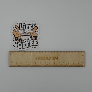 May include: A die-cut sticker featuring a coffee cup graphic with the text "LIFE HAPPENS AFTER COFFEE" in black and tan colours. The sticker is positioned above a wooden ruler that shows a measurement of approximately 7.5 cm in width.
