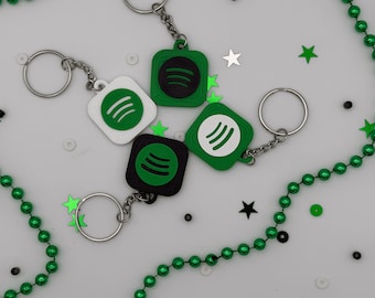 May include: Four square keychains featuring the Spotify logo. Two keychains have green bases with black logos, one has a white base with a green logo, and one has a green base with a white logo. Each keychain includes a silver metal split ring.