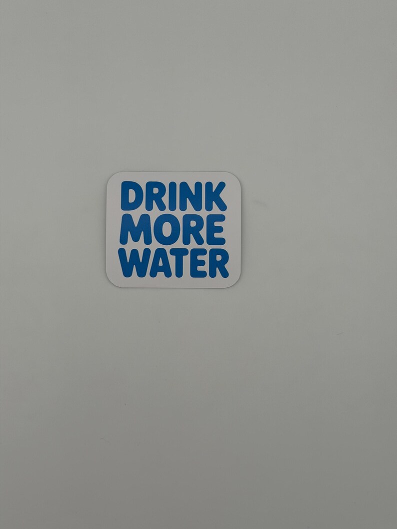 May include: A square sticker with rounded corners featuring a white background and the text DRINK MORE WATER printed in bold, blue, sans-serif capital letters. The sticker has a clean, simple design with the text centered on the surface.