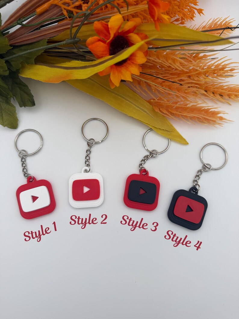 May include: Four square keychains featuring a play button icon, labeled Style 1, Style 2, Style 3, and Style 4. The keychains come in color combinations of red and white or red and black, each attached to a silver metal split ring by a short chain.