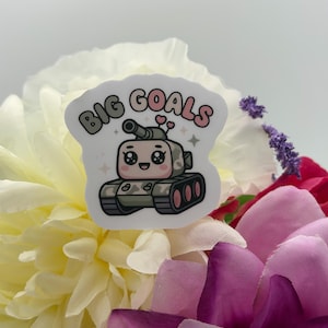 Puede incluir: Una pegatina troquelada que muestra un tanque de dibujos animados con una cara sonriente, ojos grandes y dos peque&ntilde;os corazones rosas sobre la torreta. El texto BIG GOALS est&aacute; impreso en una fuente curva y burbujeante sobre el tanque.