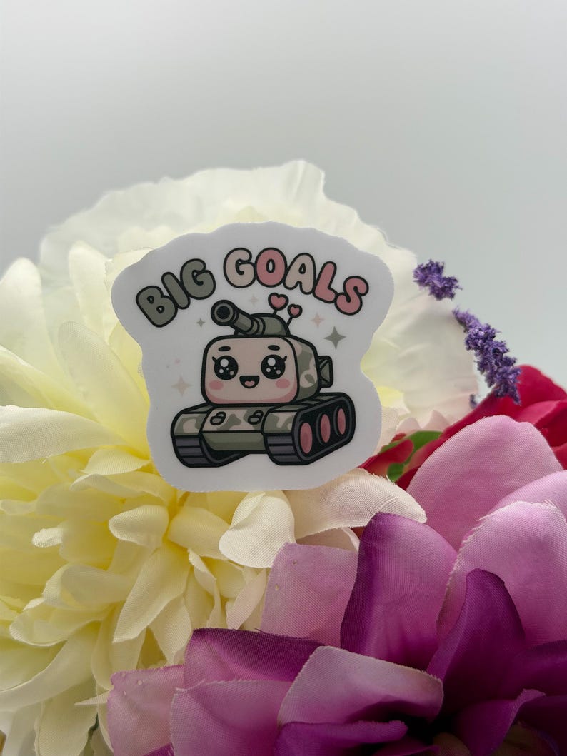 Puede incluir: Una pegatina troquelada que muestra un tanque de dibujos animados con una cara sonriente, ojos grandes y dos peque&ntilde;os corazones rosas sobre la torreta. El texto BIG GOALS est&aacute; impreso en una fuente curva y burbujeante sobre el tanque.