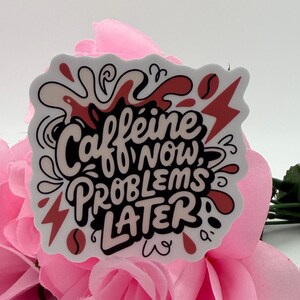 Puede incluir: Una pegatina troquelada con el texto en negro Caffeine NOW, PROBLEMS LATER. El dise&ntilde;o incluye salpicaduras de l&iacute;quido abstractas, granos de caf&eacute; y formas de rayos rojos sobre un fondo blanco, creando una visualizaci&oacute;n gr&aacute;fica y audaz.