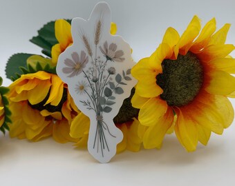 Puede incluir: Una pegatina troquelada con una ilustración botánica de un ramo de flores silvestres con espigas de trigo, pequeñas flores blancas y hojas de eucalipto verdes, atadas con un cordel fino, sobre un fondo de girasoles amarillos.