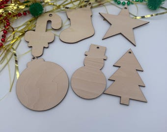 May include: A set of five unfinished light-colored wooden ornaments in the shapes of a candy cane, a stocking, a star, a round bauble, and a snowman, alongside a triangular tree shape, each featuring a small hole for hanging.