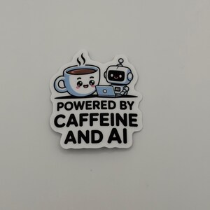 May include: A die-cut sticker featuring a cartoon illustration of a smiling coffee cup and a small robot working on a laptop. The text below the characters reads POWERED BY CAFFEINE AND AI in bold black capital letters against a white background.