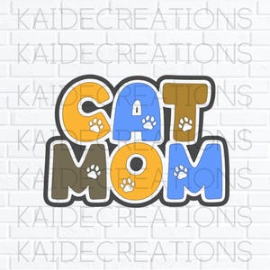 May include: A multi-colored graphic design featuring the text CAT MOM in bold, blocky letters. The letters are colored in shades of yellow, blue, and brown, with small white paw print icons scattered across the characters and a black outline.