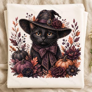 Puede incluir: Una sudadera de color crema con una ilustración gráfica de un gato negro que lleva un sombrero de bruja oscuro con una rosa morada y un lazo a juego. El gato está rodeado de elementos otoñales que incluyen calabazas y flores oscuras.
